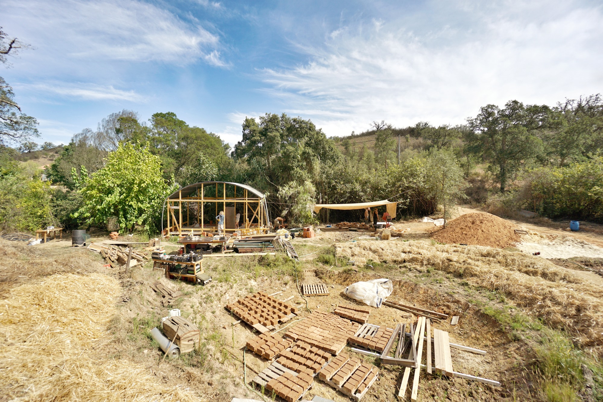 Natural building site with timber-frame structure and field of drying adobe bricks