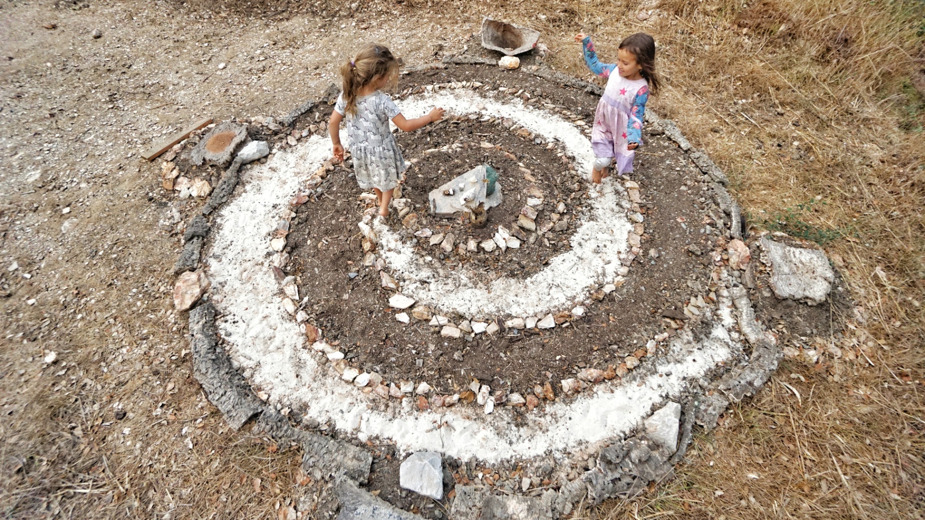 Two children playing on a stone spiral altar on the land.